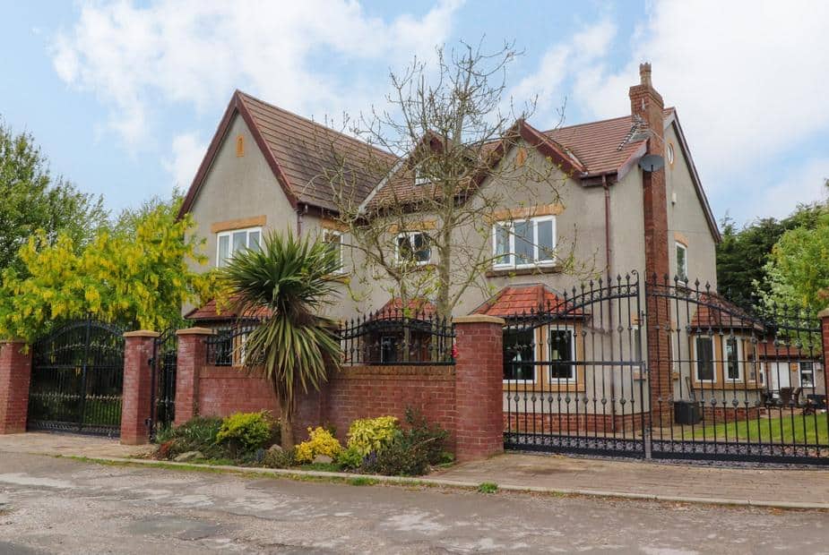 Linwood with red brick wall, wrought iron gates and front garden with palm tree.