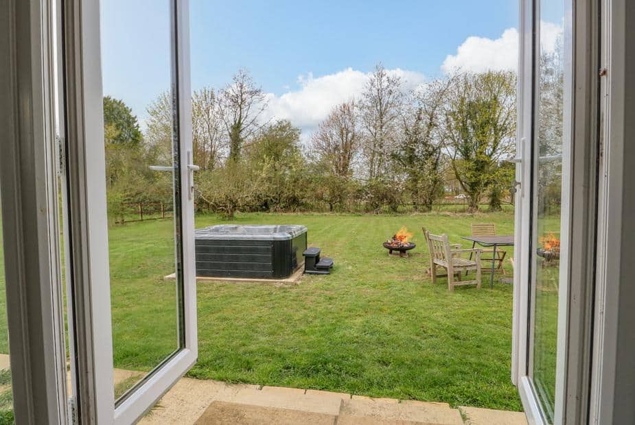Cottage garden with hot tub, fire pit and outdoor seating seen through open doors