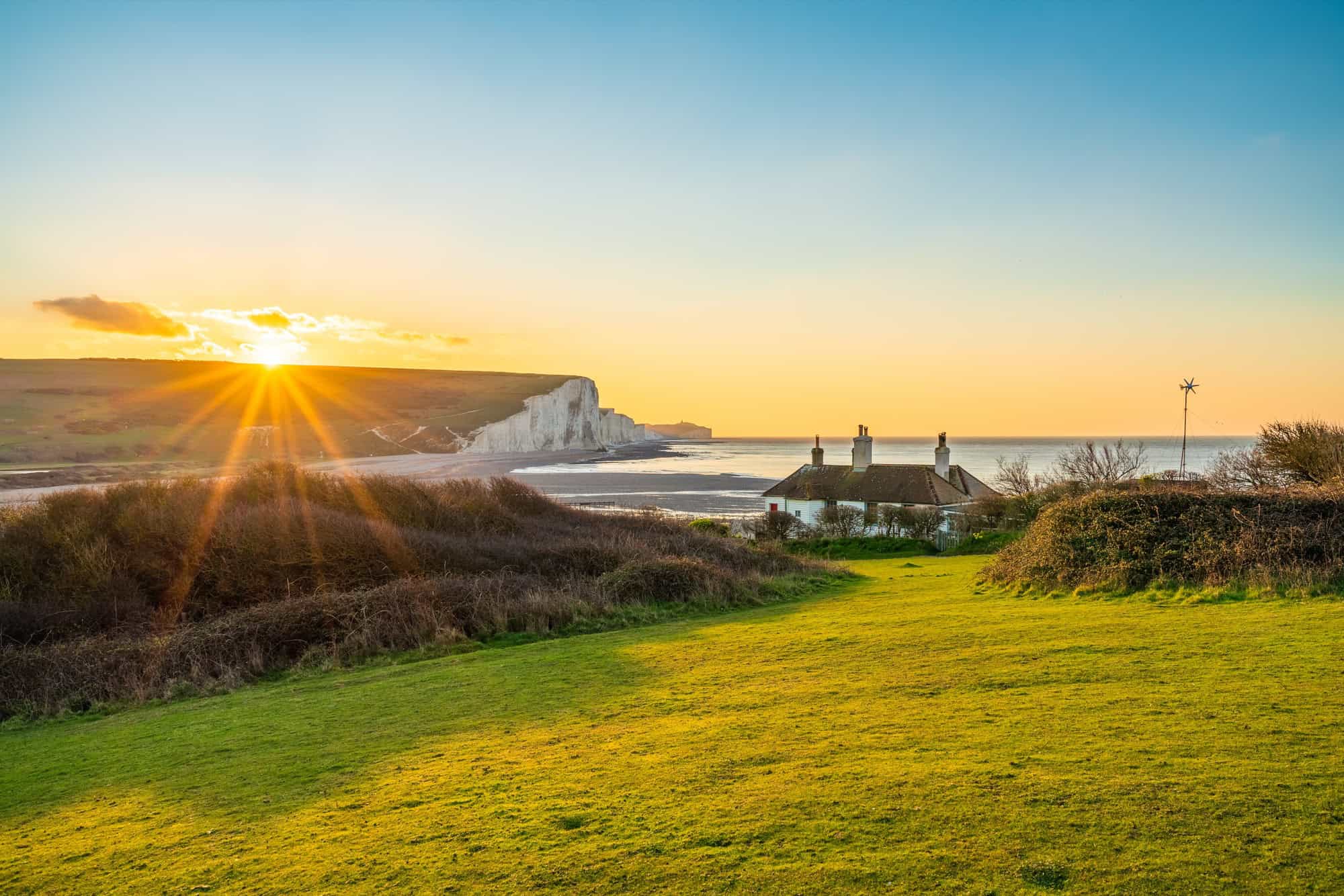 Sunrise sunburst shining over the Coastguard Cottages and the white chalk cliffs of the Seven Sisters on the South Coast.