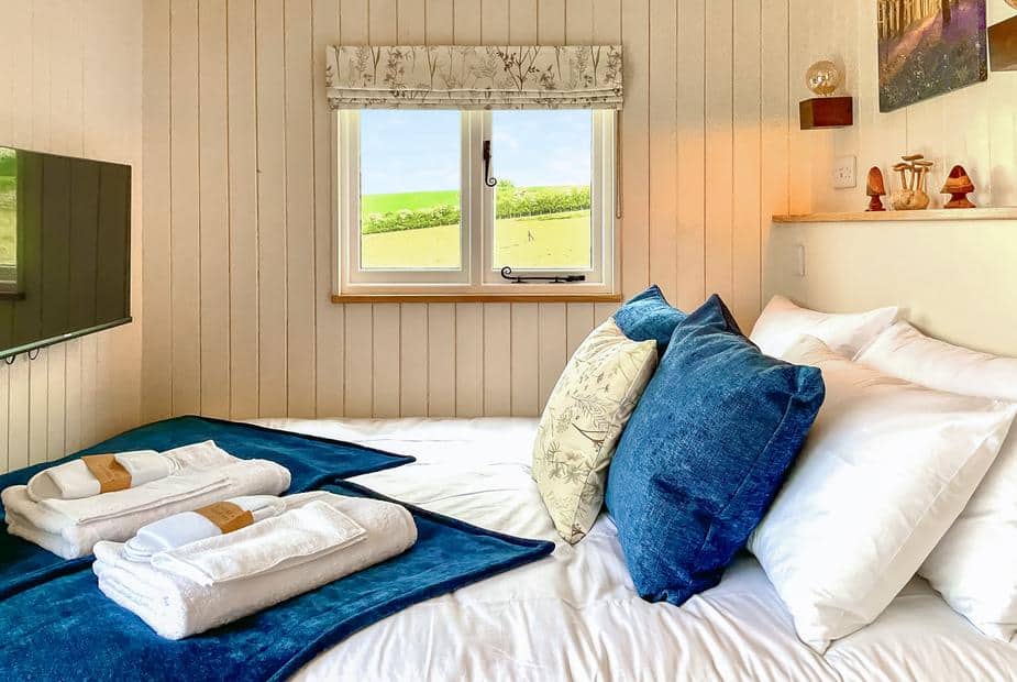 Lodge bedroom with double bed, blue cushions, window view, and TV on the wall