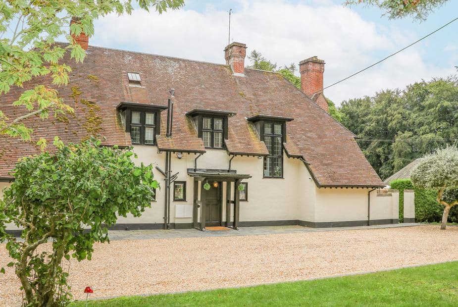 Little Picket cottage with steep tiled roof and gravel driveway in front garden.