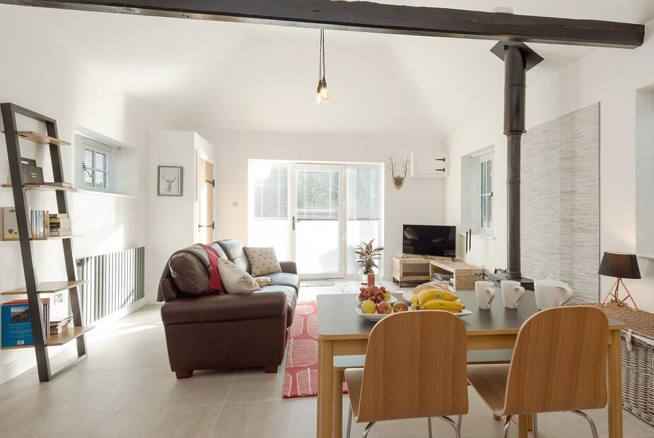 Cottage living area with woodburner, dining table and sofa facing TV