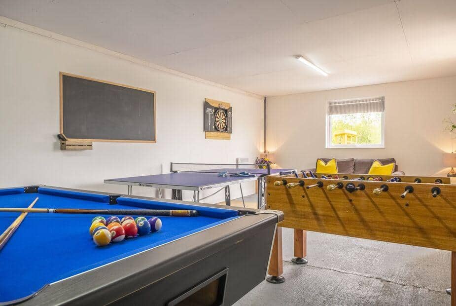 Cottage games room with pool table, table tennis, foosball, dartboard, and sofa.