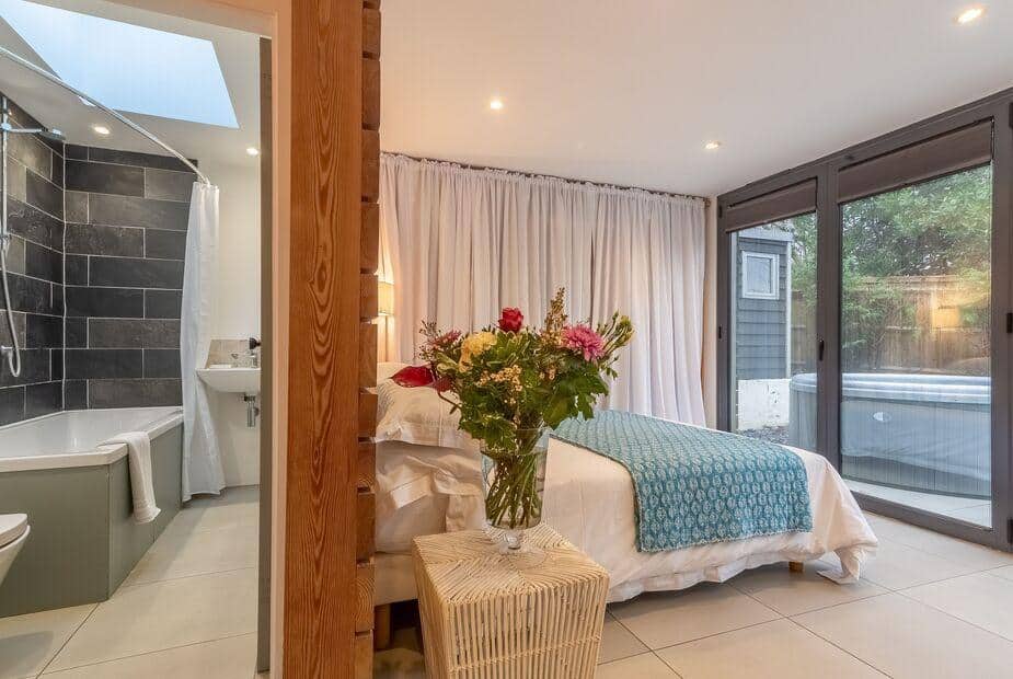 Cottage bedroom with vase of flowers, ensuite bathroom, and glass doors to patio