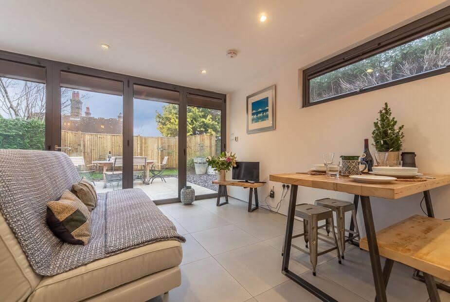 Cottage living area with sofa, dining table and doors opening to garden patio with seating