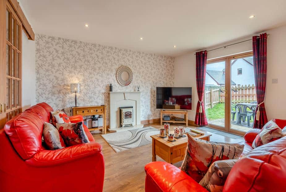 Cottage lounge with red sofas, fireplace and sliding doors to garden patio with chairs