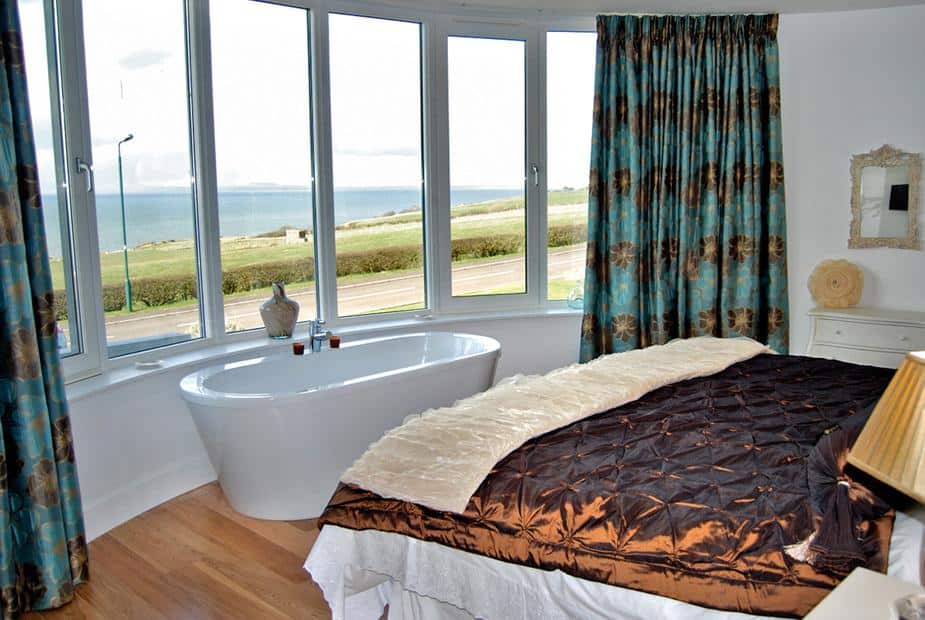Cottage bedroom with freestanding bath beside bay window and sea view