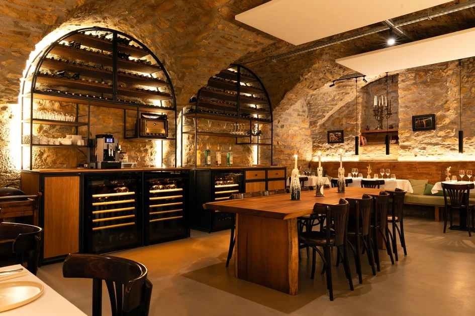 Intérieur chaleureux de restaurant avec murs en pierre, grandes étagères à vin, table en bois avec bougies, et chaises sombres.