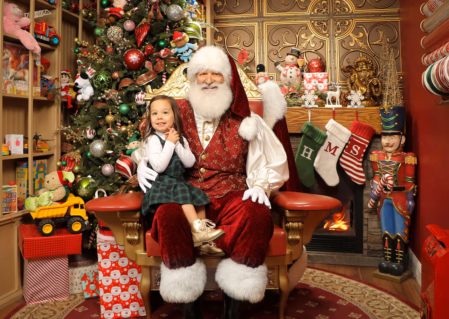Young girl sitting with real-bearded Santa in decorated studio with Christmas tree and fireplace