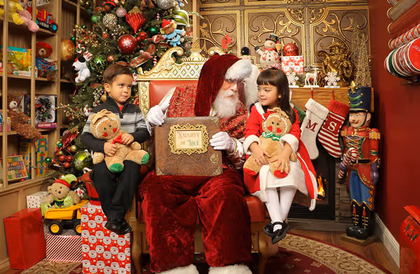 Family of four with Santa on throne surrounded by wrapped presents and Christmas decorations