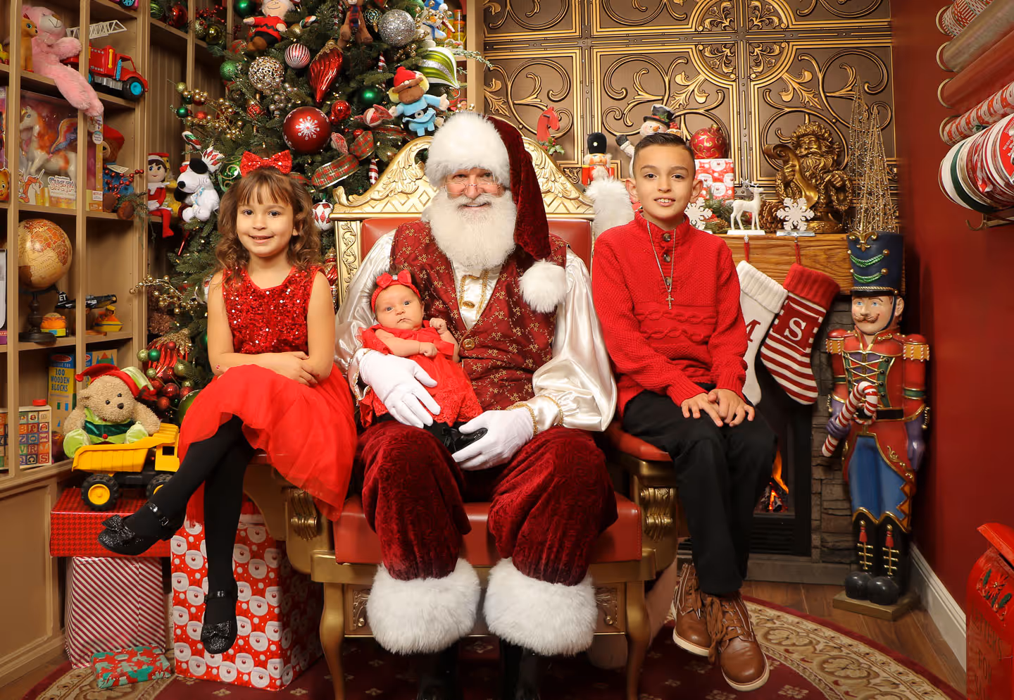Smiling young siblings with Santa holding their newborn baby system in a festively-decorated photo studio
