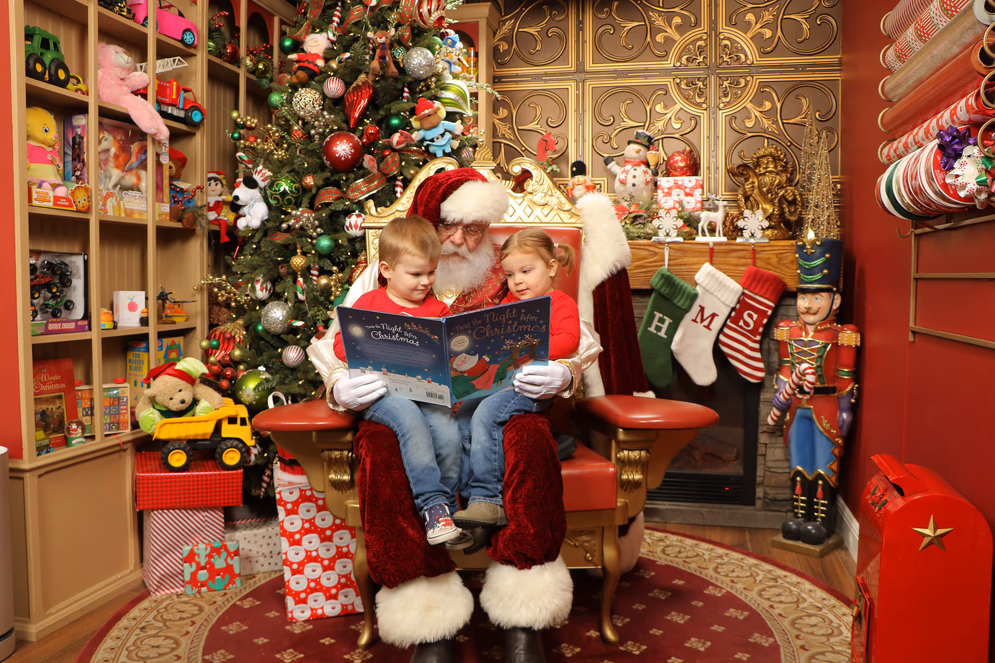 Two young kids on Santa's lap while he reads 'Twas the Night Before Christmas to them