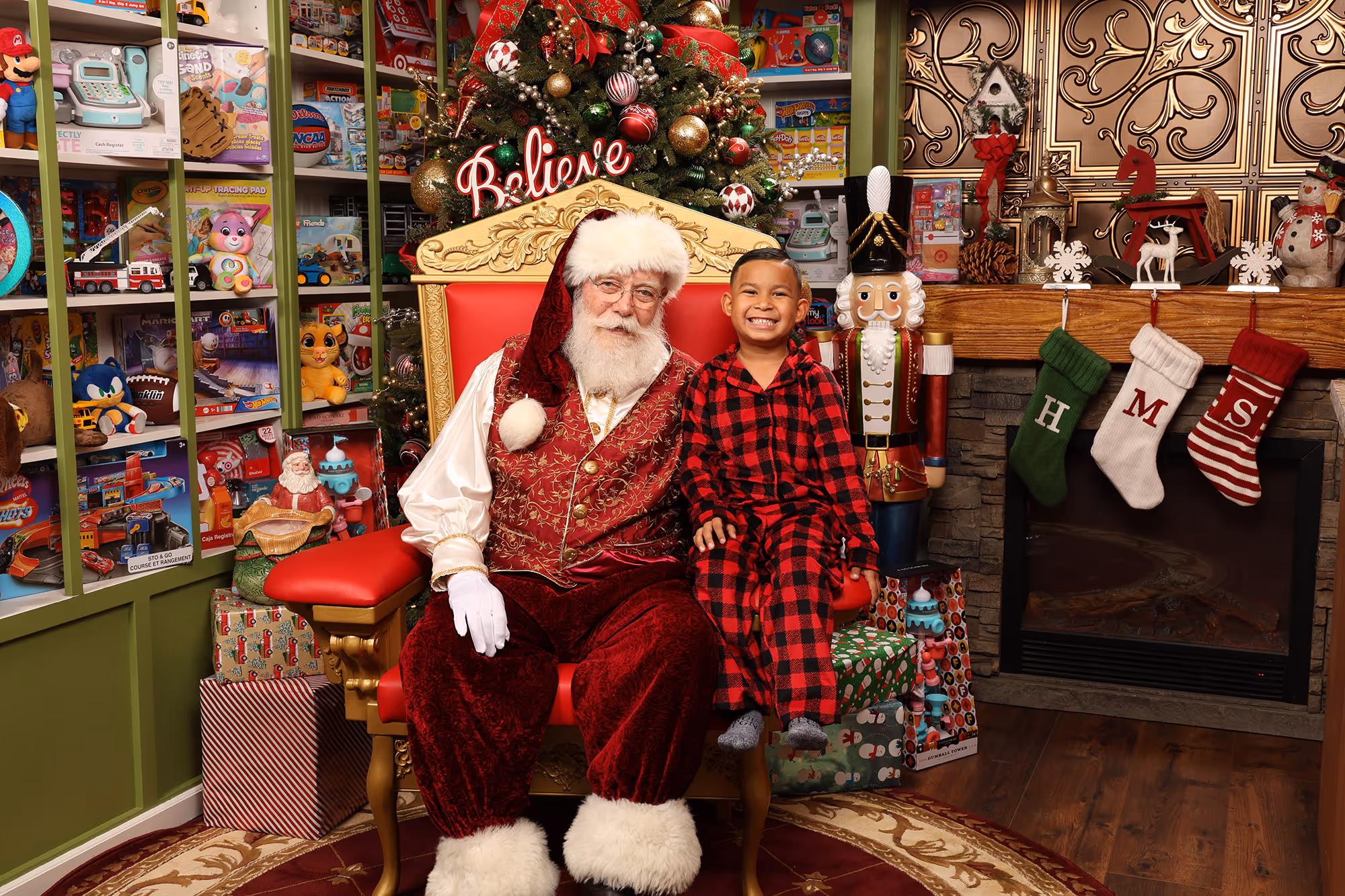 Smiling boy in Christmas pajamas pictured with Santa in a festive photo studio