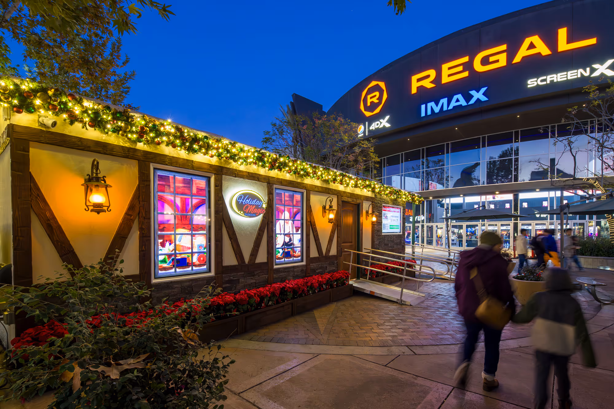 Holiday Magic Studios exterior at dusk with illuminated garland, lit windows and poinsettia flowers