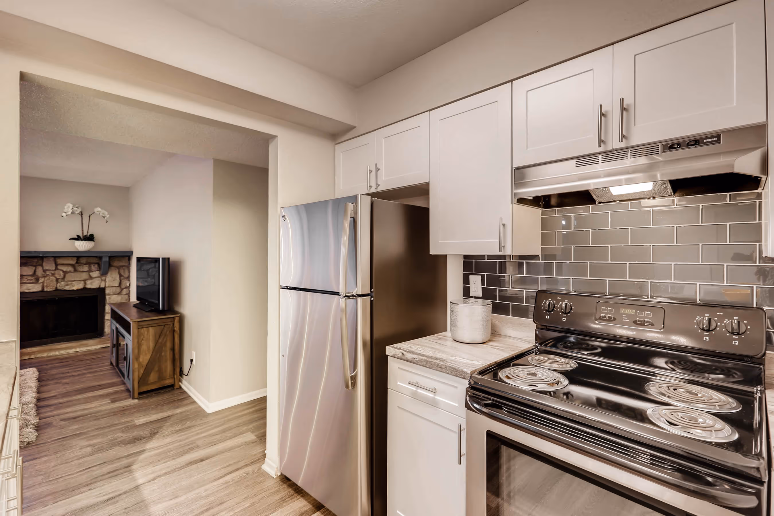 Modern kitchen with a stainless steel refrigerator, white cabinets, and a gray subway tile backsplash, in an apartment at Villas at Holly in Centennial, CO.