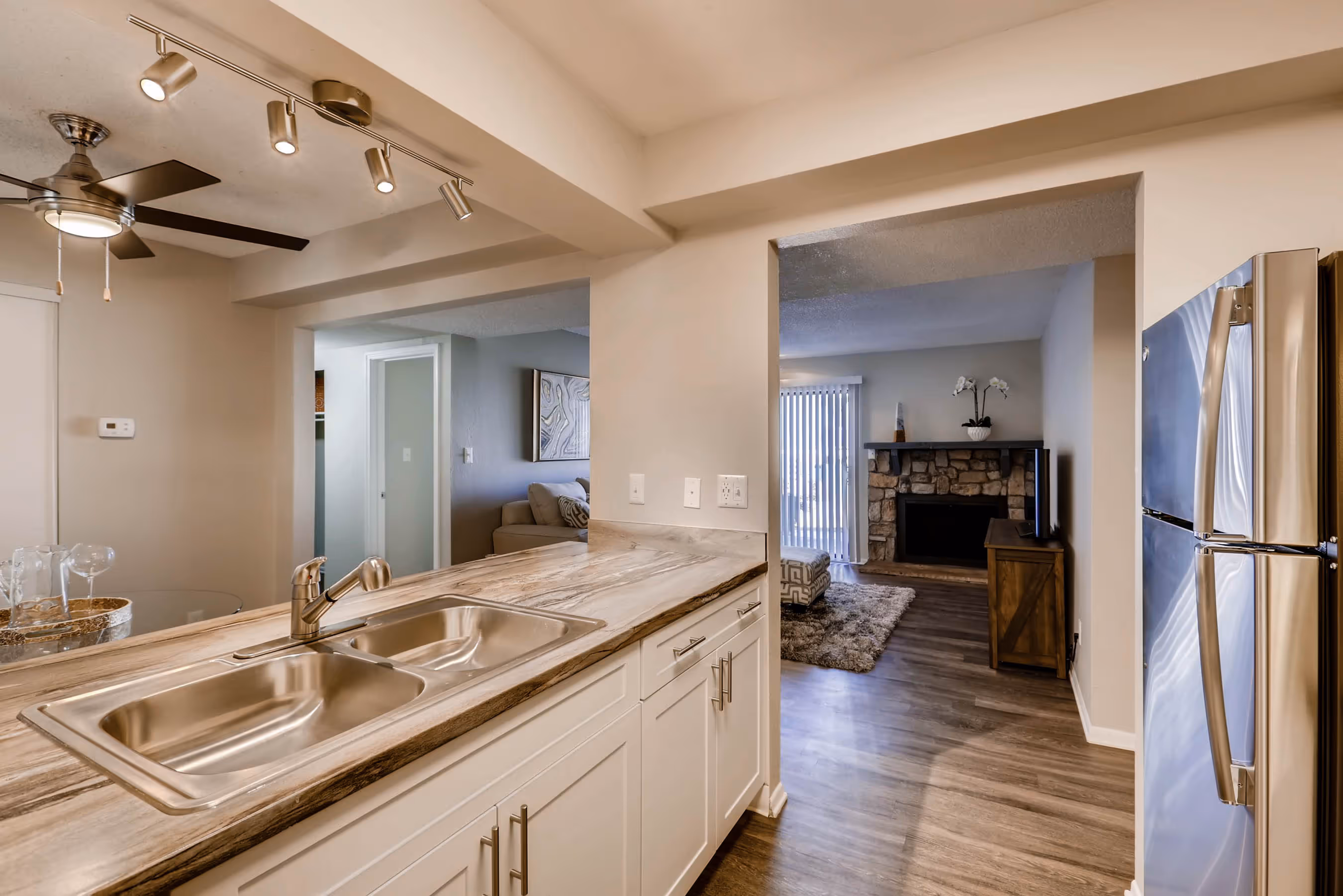 Apartment kitchen with a large stainless steel refrigerator, white cabinets, and an open view into the living room with a fireplace, at Villas at Holly in Centennial, CO.