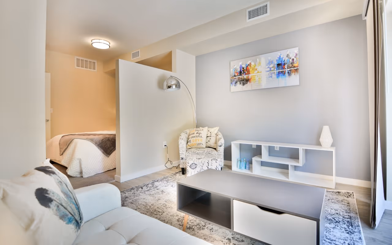 Spacious studio apartment living area with a partial wall divider, a sofa, and a view into the bedroom, at Villas at Holly in Centennial, CO.