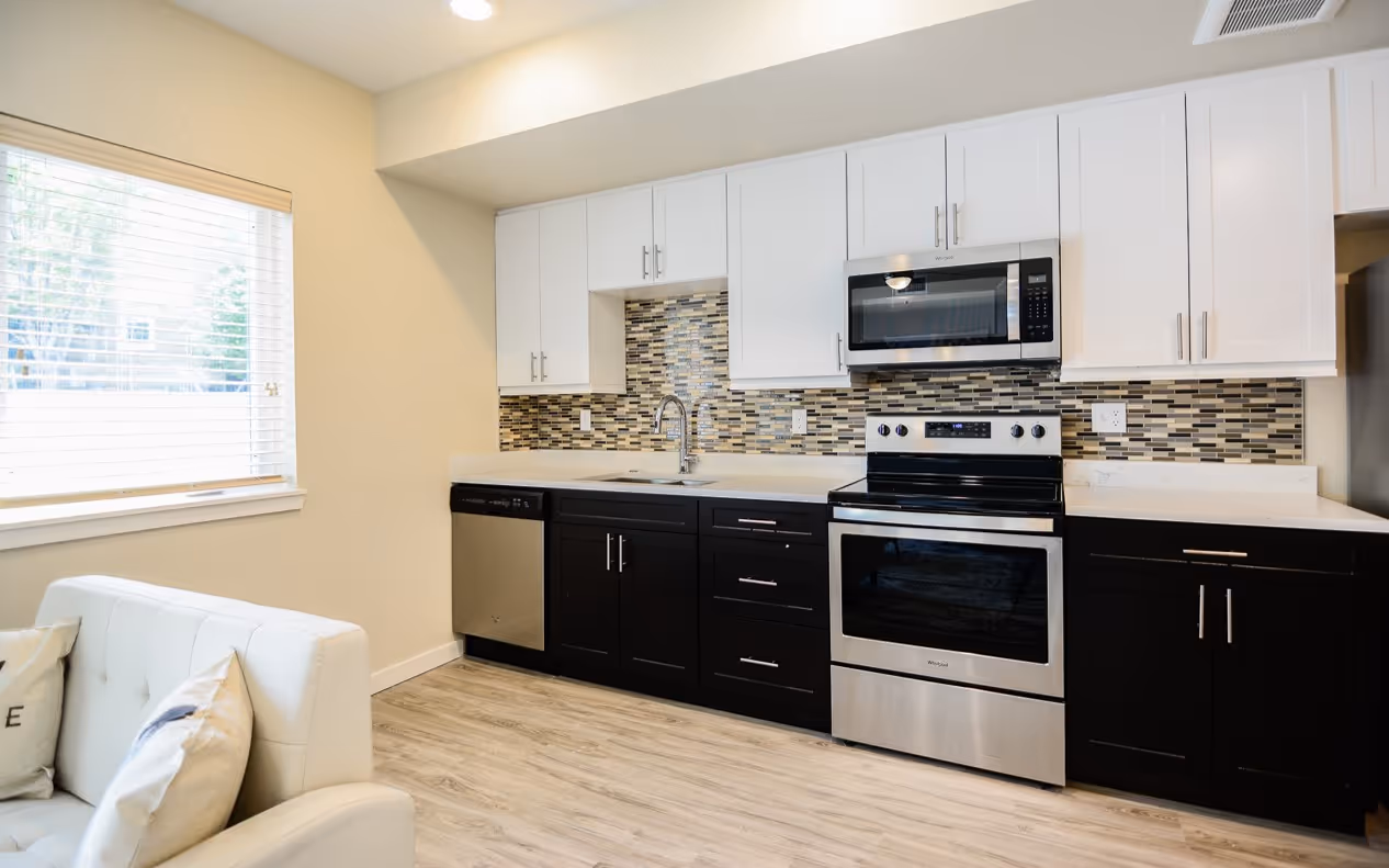 Modern studio apartment kitchen with two-tone cabinetry, stainless steel appliances, and a mosaic tile backsplash, at Villas at Holly in Centennial, CO.