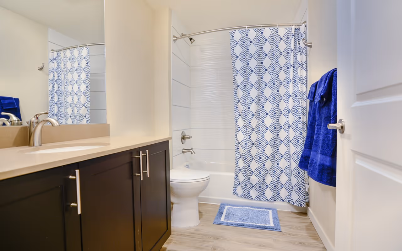 Modern bathroom with a dark wood vanity, white countertop, and a shower/tub with a blue patterned curtain, in a studio apartment at Villas at Holly in Centennial, CO.
