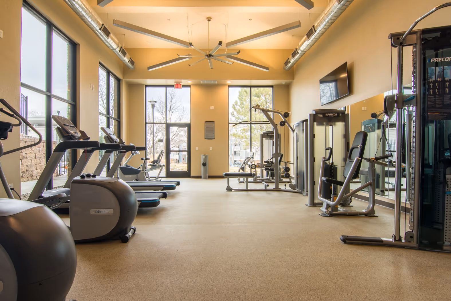 Spacious and well-lit resident fitness center with a variety of cardio machines, free weights, and large windows at Villas at Holly in Centennial, CO.