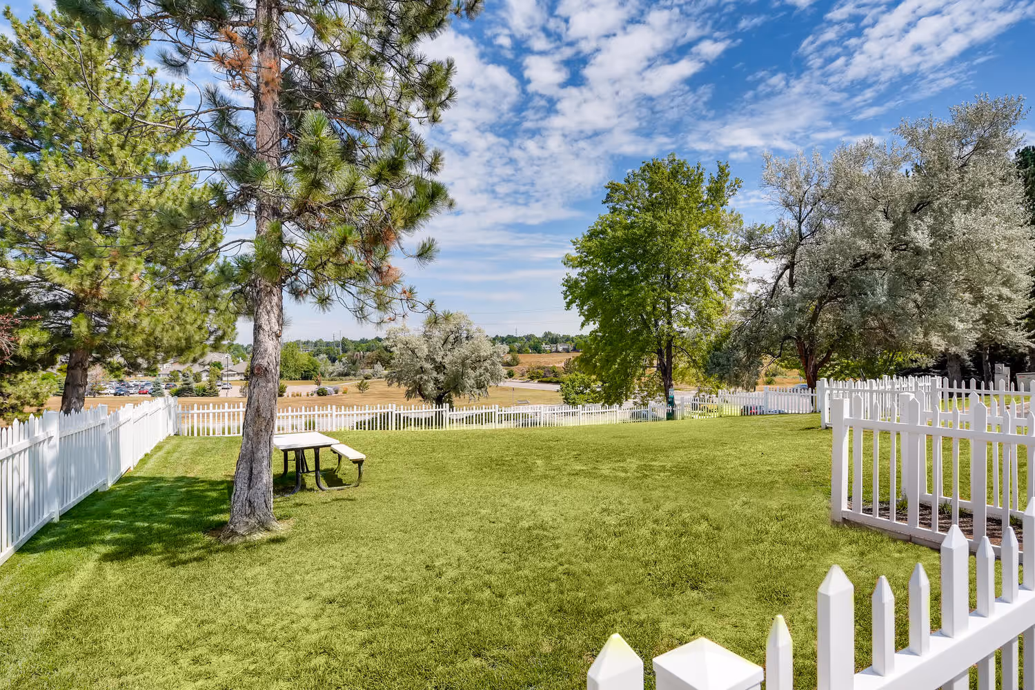 Spacious community park with a picnic table and white picket fence, providing green space for residents at Villas at Holly in Centennial, CO.