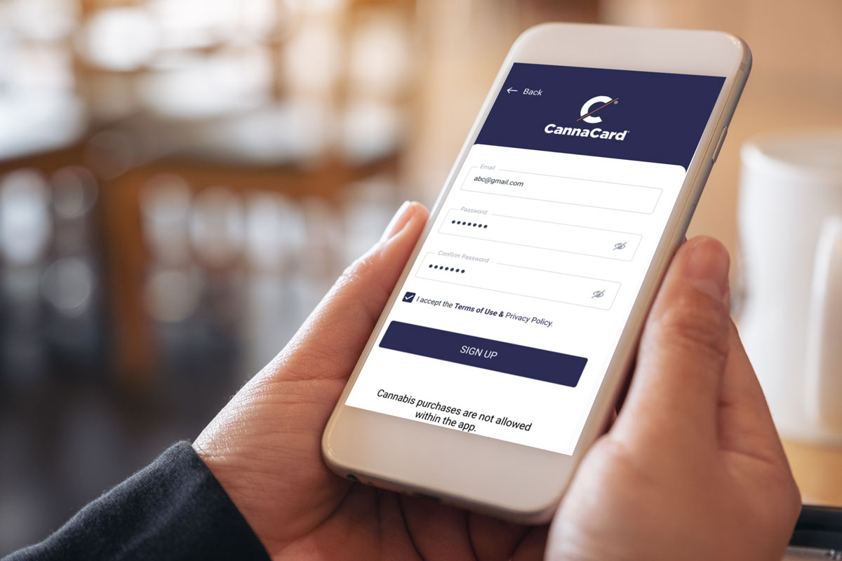 Two hands holding a cellphone displaying CannaCard app registration screen