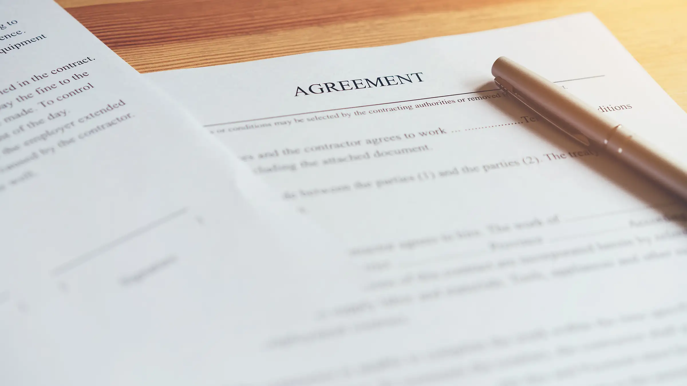 Close-up of an agreement document with a pen resting on it on a wooden surface.