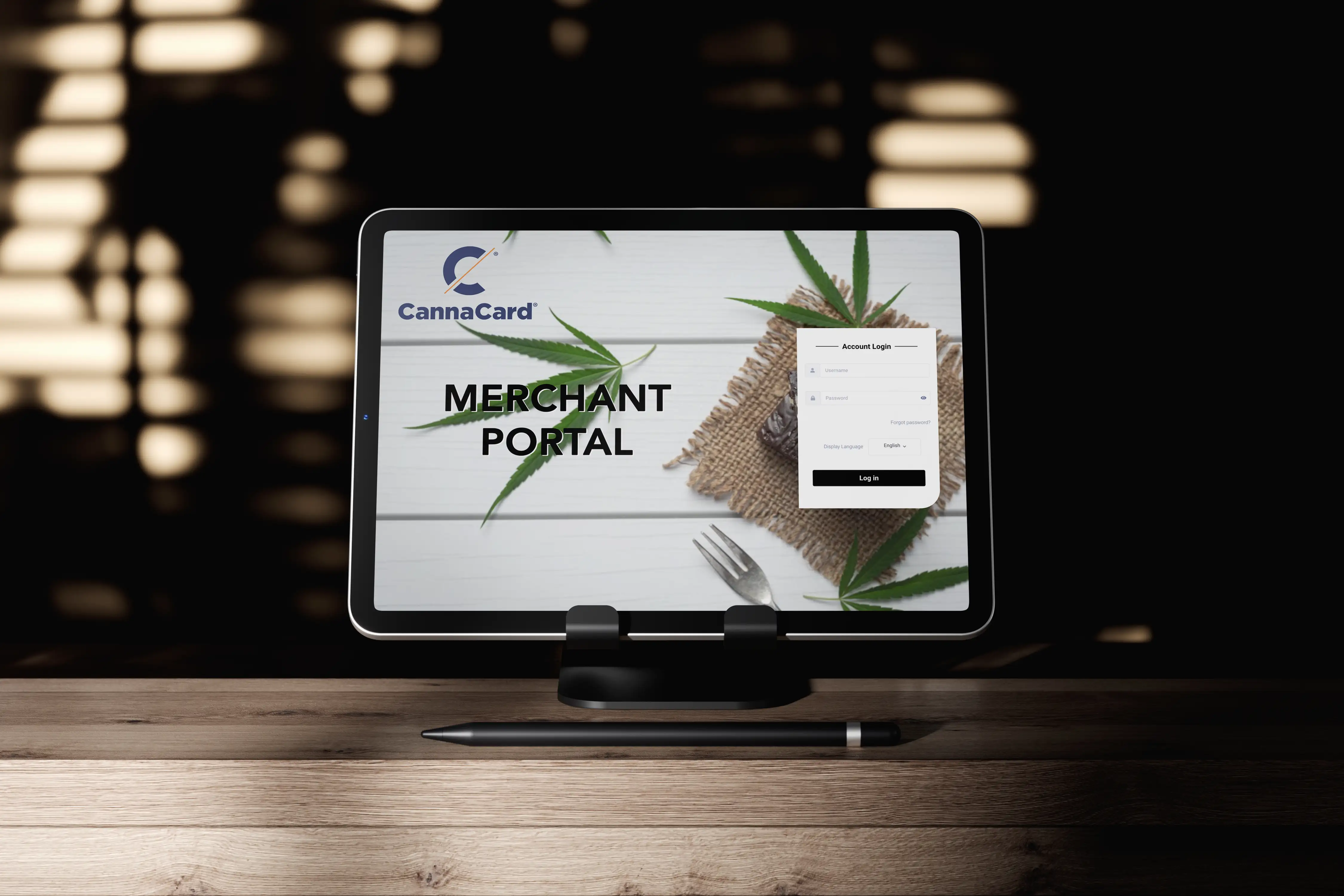Tablet on stand displaying CannaCard merchant portal login screen with cannabis leaves and a fork in the background.