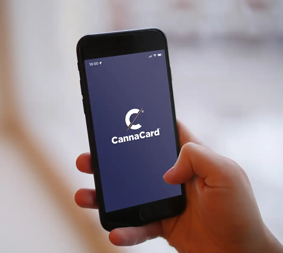 Hand holding a smartphone displaying the CannaCard app logo on screen.