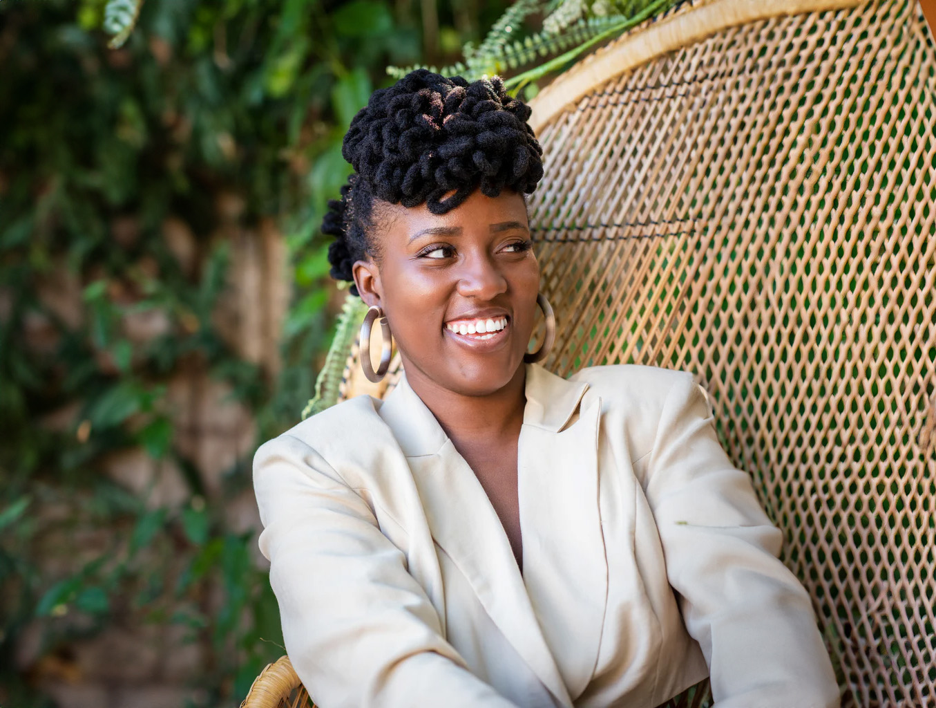 Imani Cowrie sitting on a chair posing with her earrings.