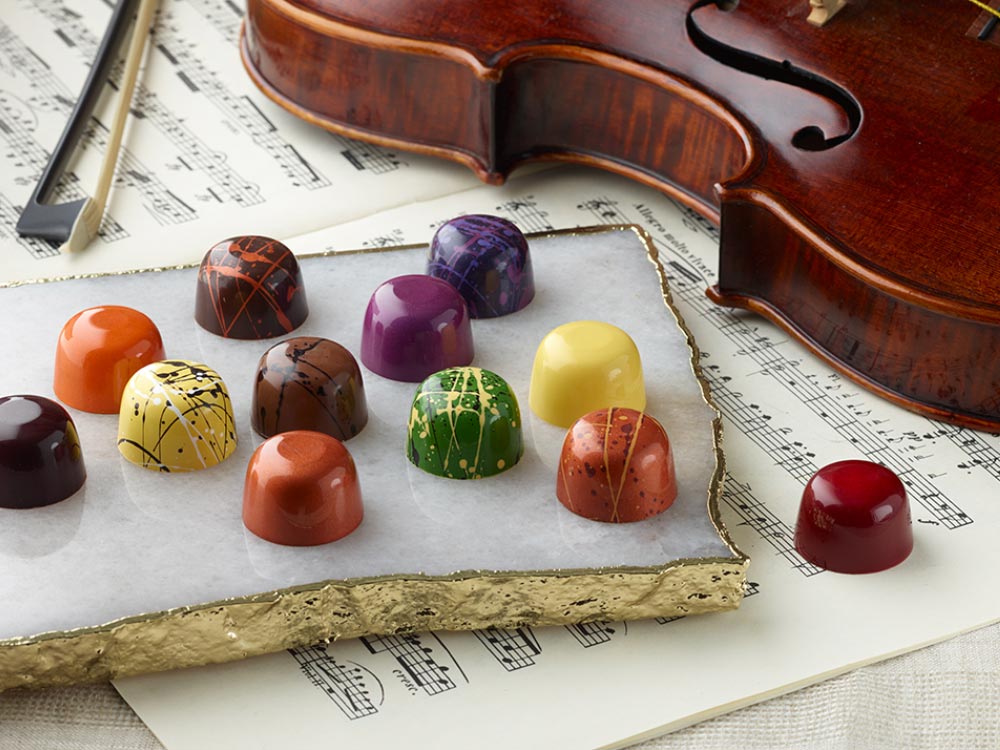 Assortment of brightly colored truffle chocolates with violin in background.