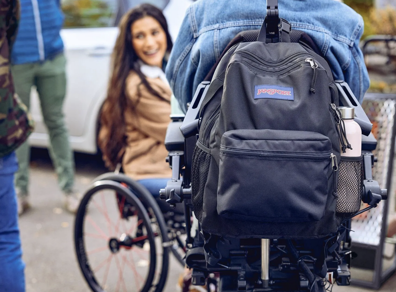 Wheelchair user showing an up close black Jansport backpack holding various items.