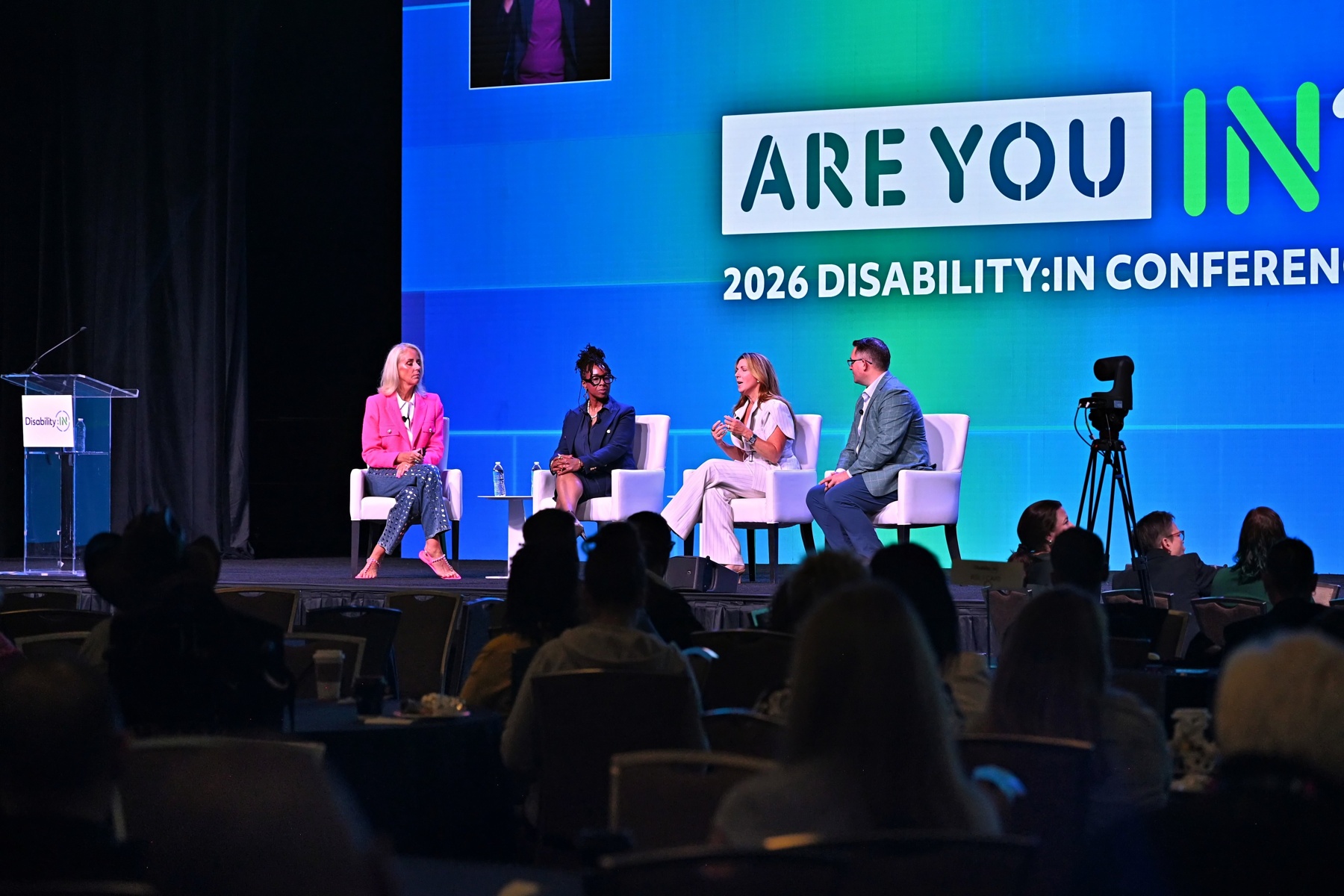 A panel of speakers onstage during the global Disability:IN conference. A full audience watches intently.