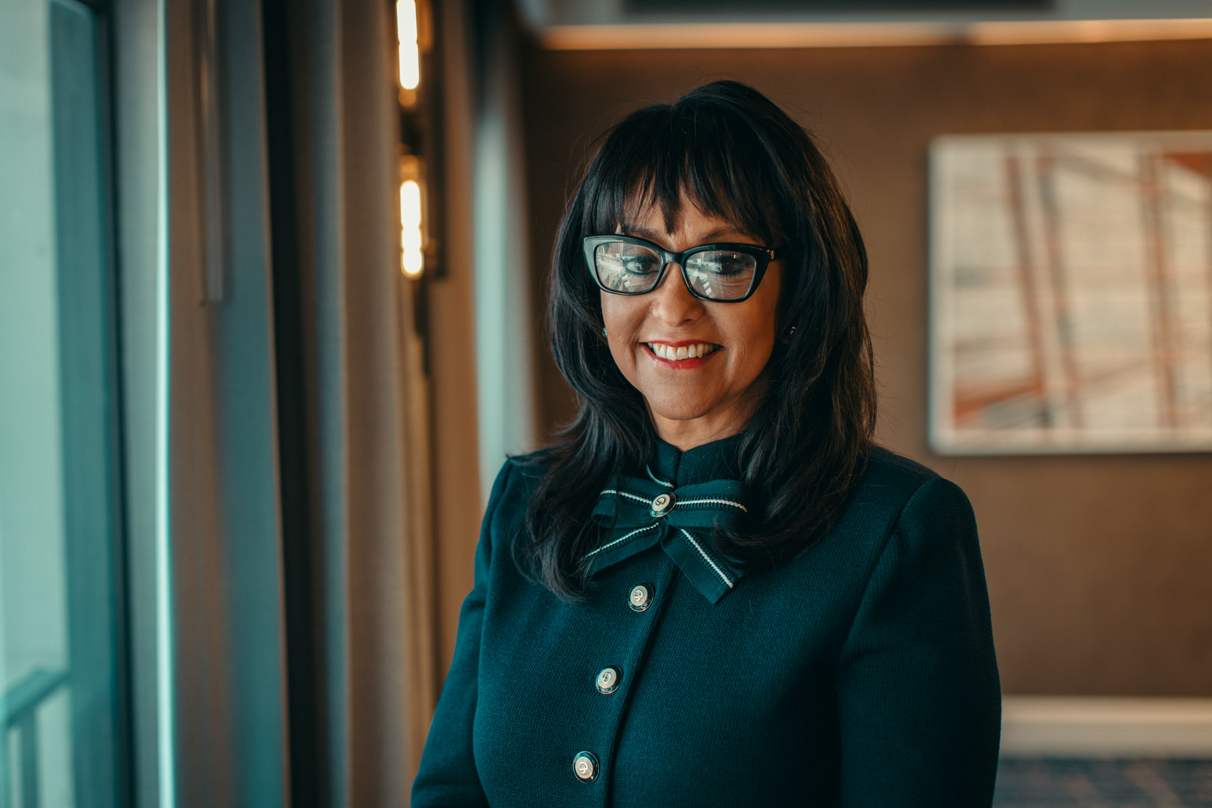 Artura Taylor smiles in an office. She wears glasses and a dark blue suit.