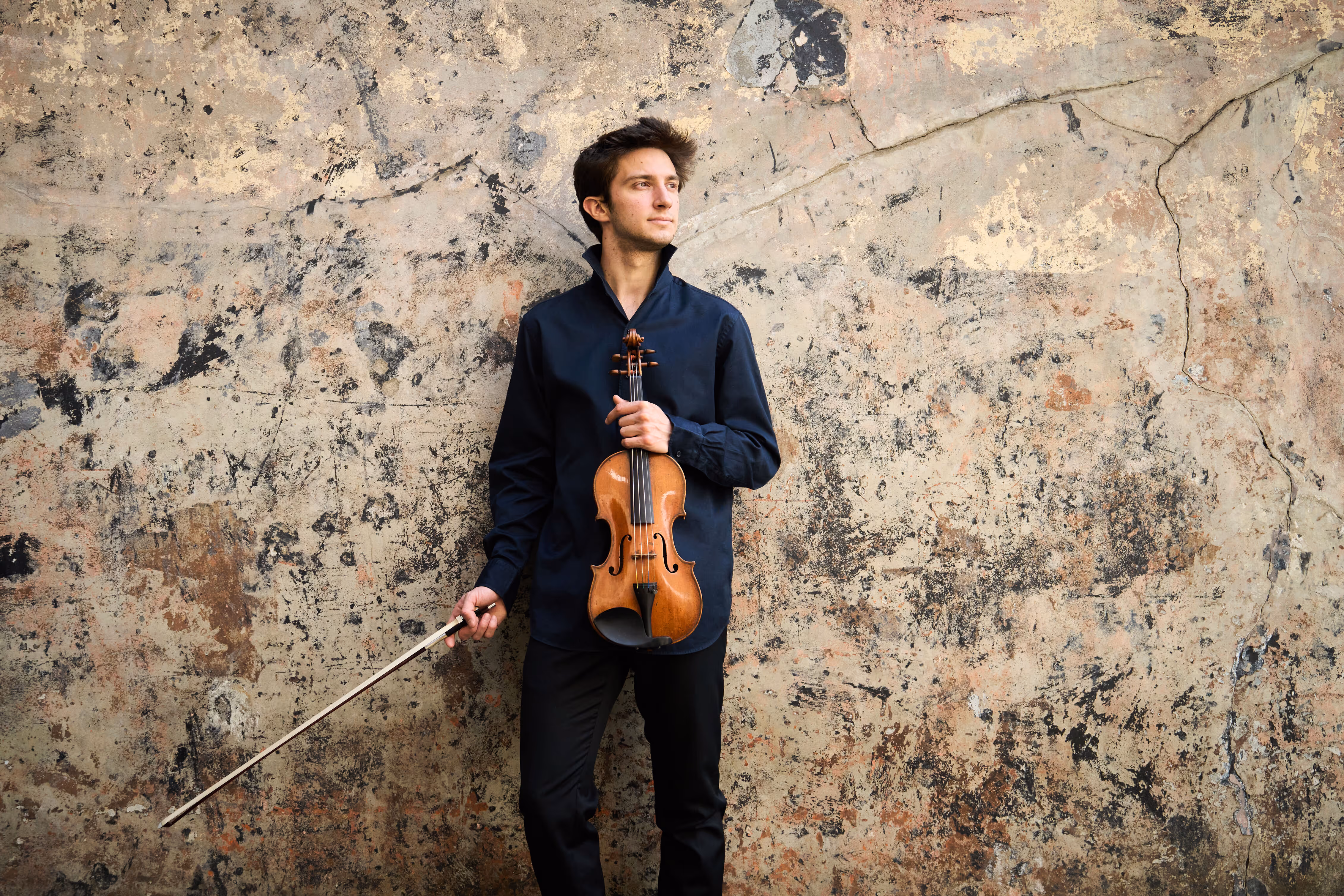 Matteo holding his violin in front of a colour wall