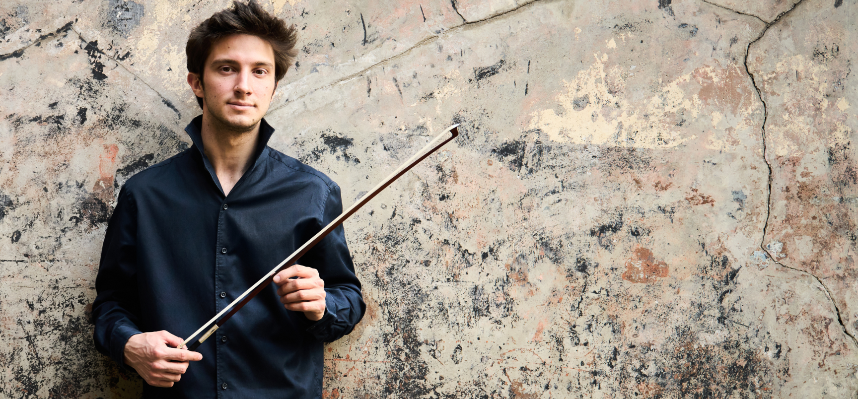 Matteo in front of a colourful wall holding his bow