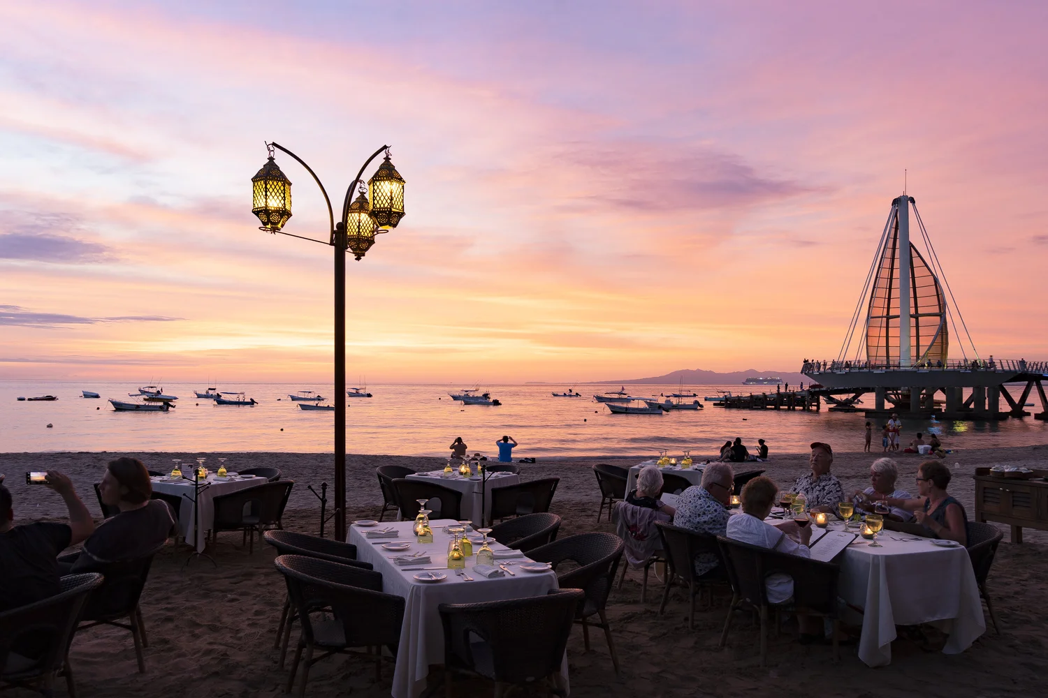 Candlelit tables on the sand at La Palapa at sunset, with the Los Muertos pier in the background