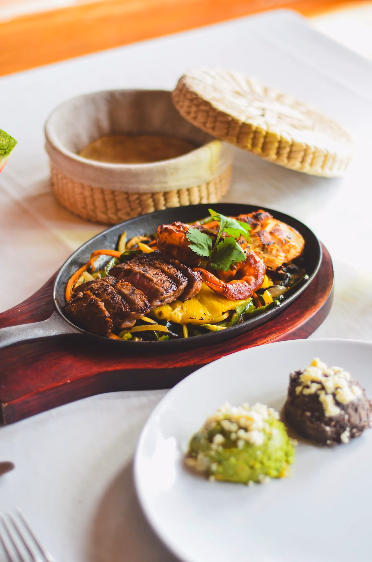 A sizzling skillet of grilled meat with guacamole and tortillas