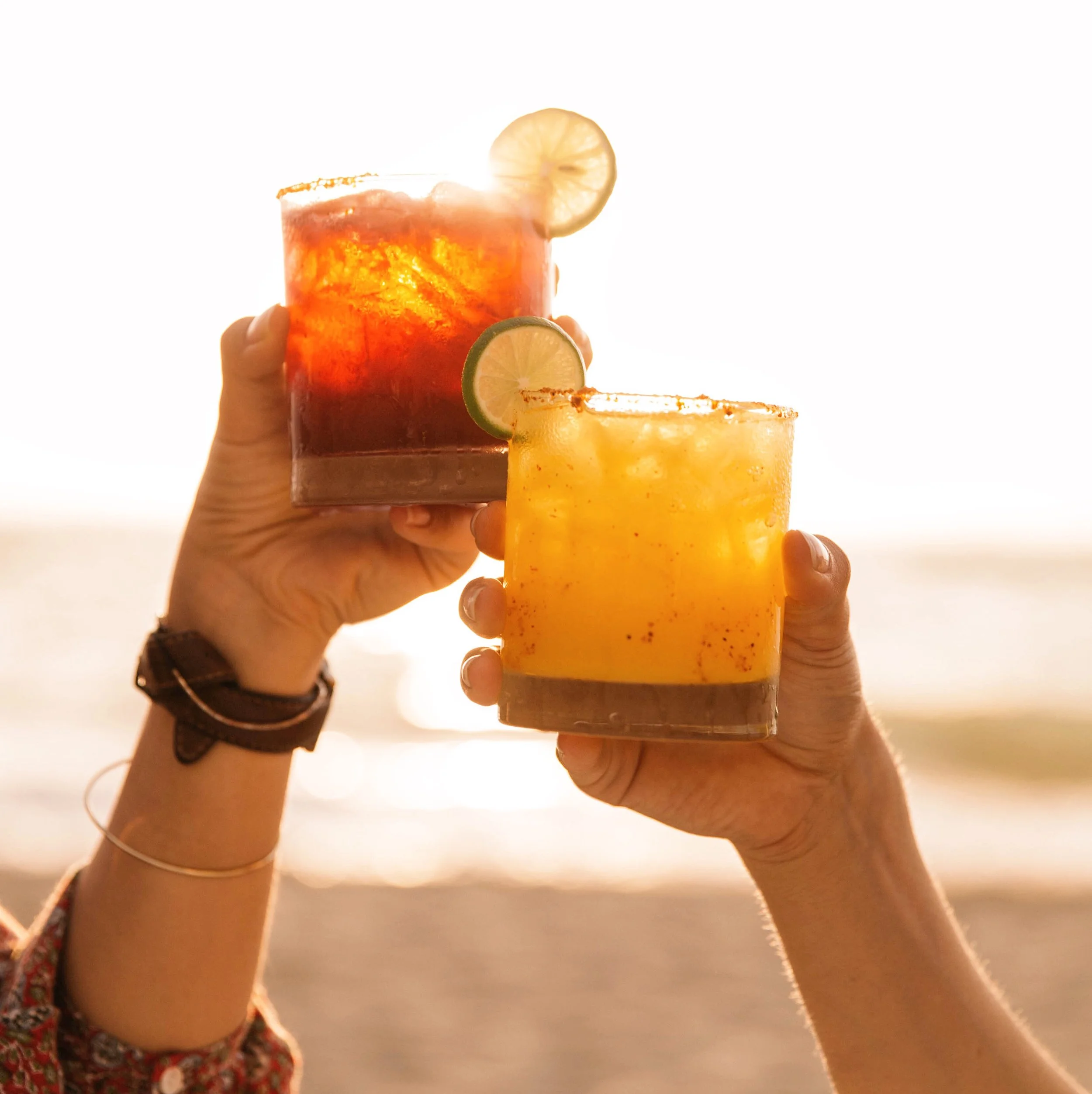 Two cocktails raised on the beach at golden hour