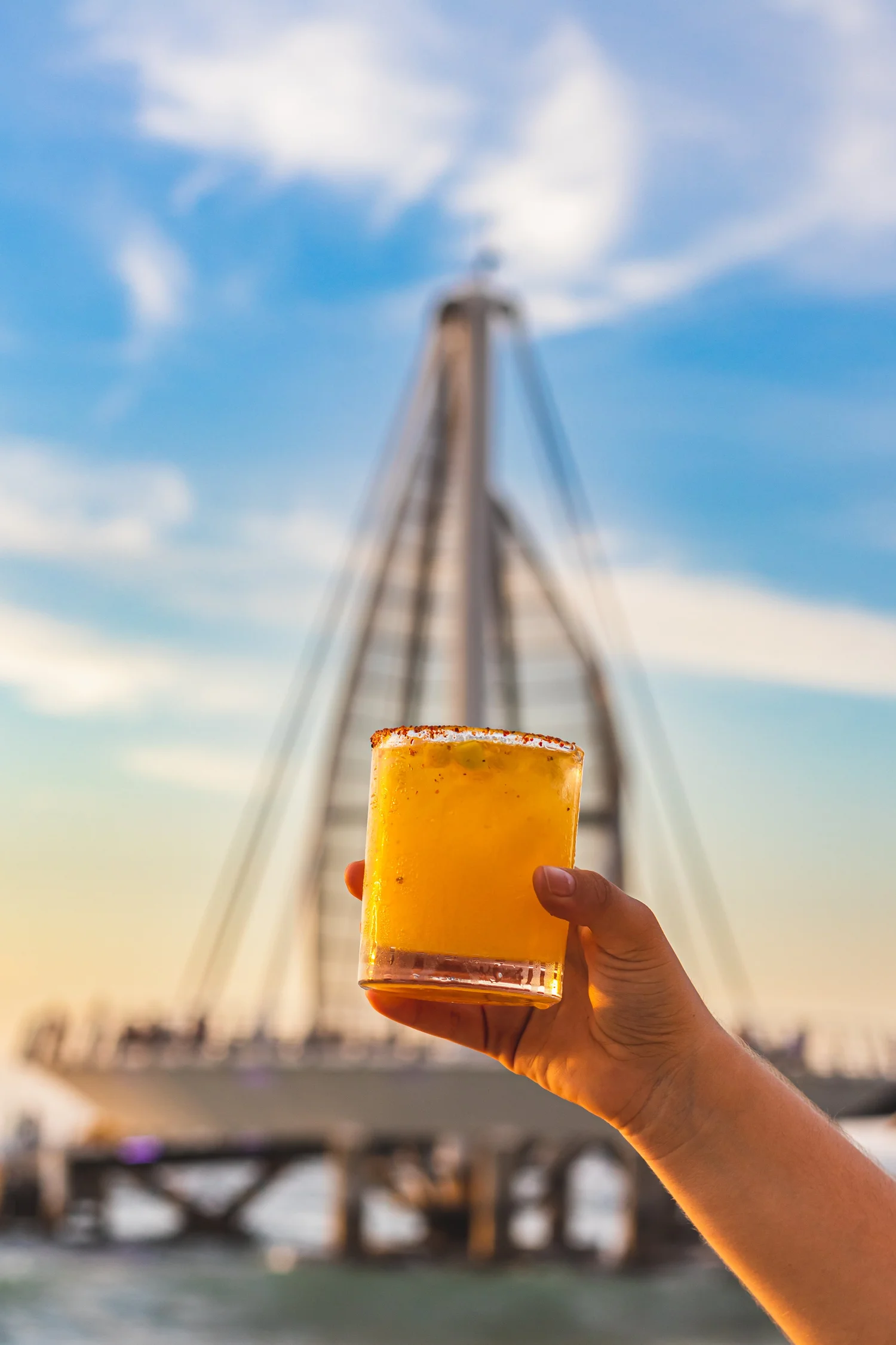 A cocktail raised in front of the Los Muertos Pier