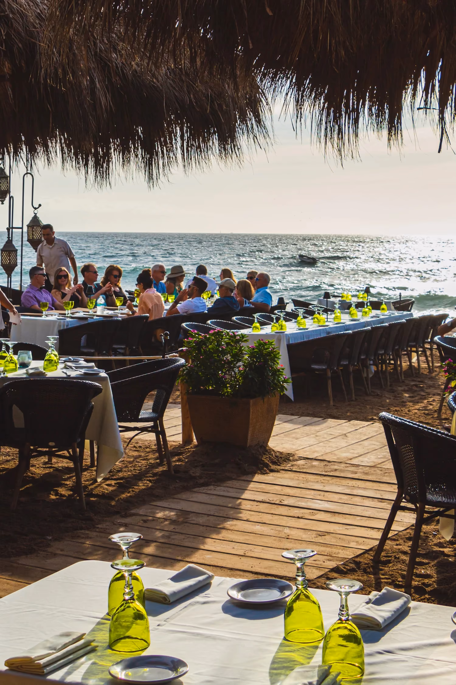 Guests at tables under the palapa facing the sea