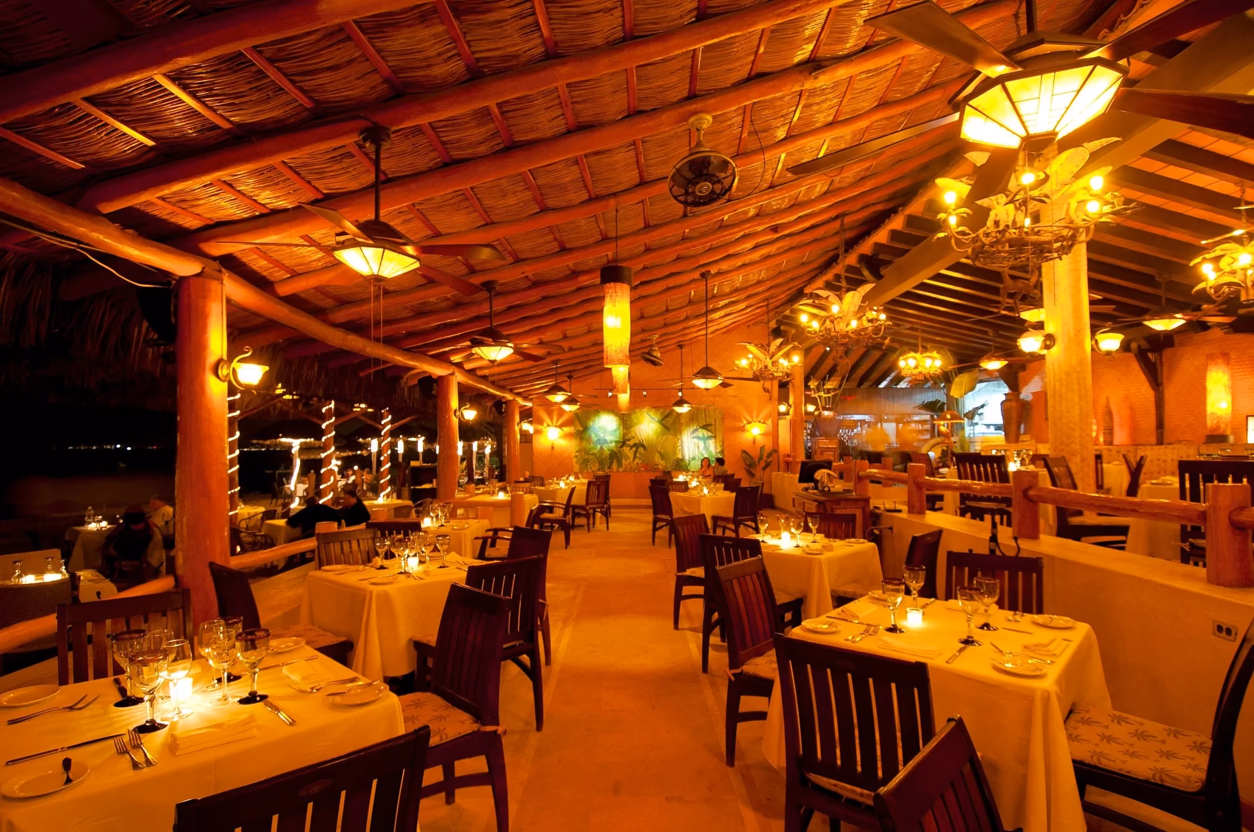 La Palapa's dining room under the thatched palapa roof, with tables set for dinner