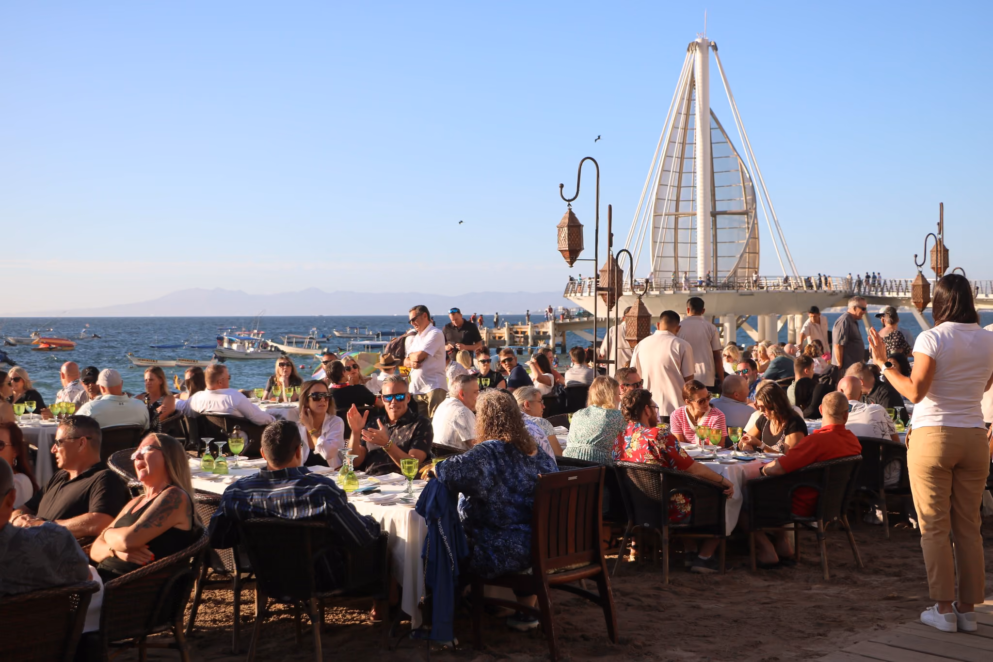 Guests at a large group dinner on the sand beside the Los Muertos pier