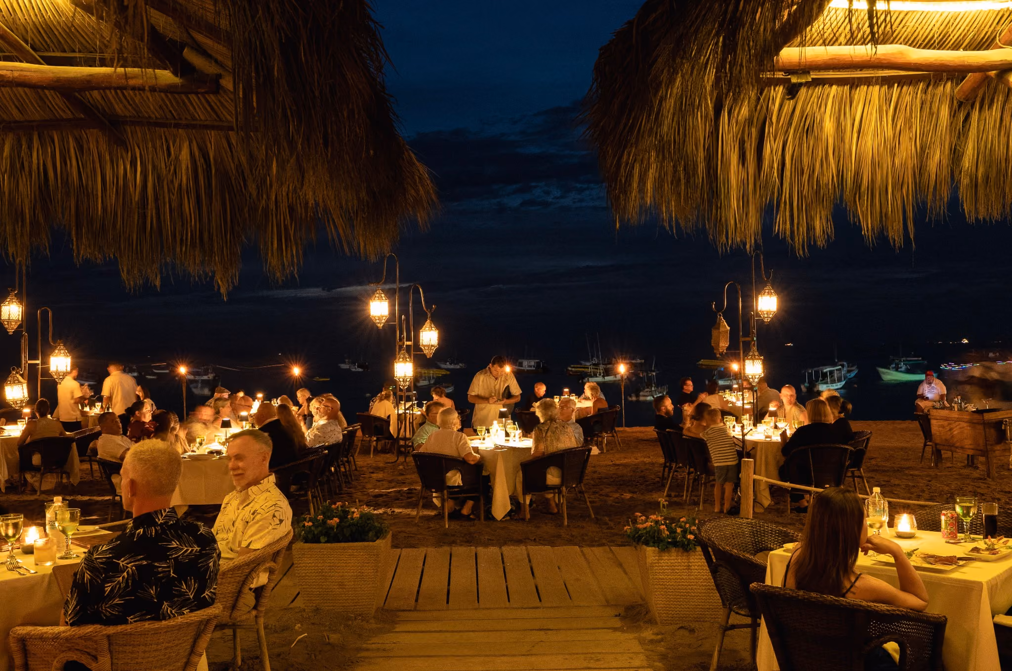 Guests dining by candlelight on the sand under the palapa at night