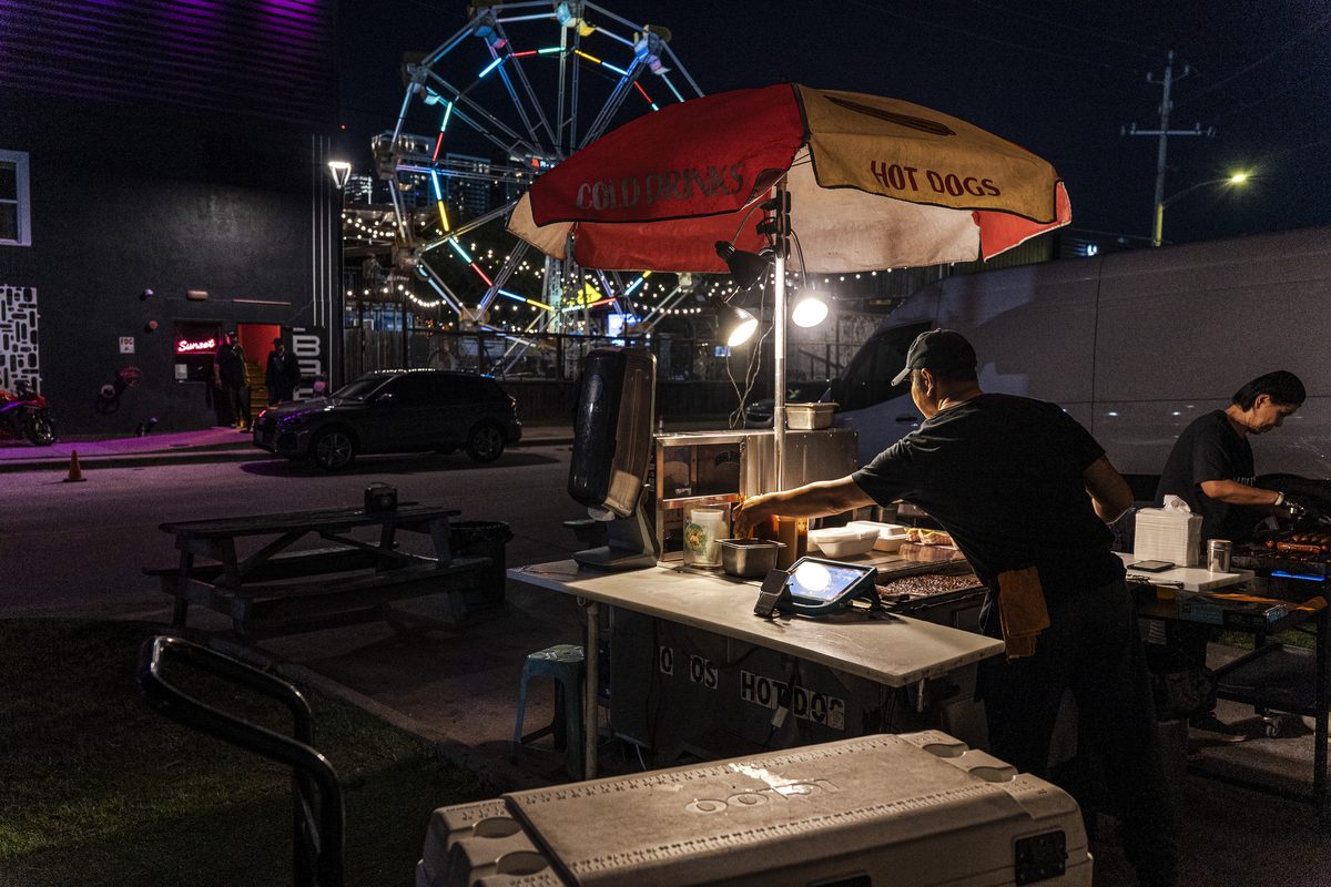 Yoyo's Hotdog cart at night in Houston, lit under a striped umbrella with a ferris wheel behind it