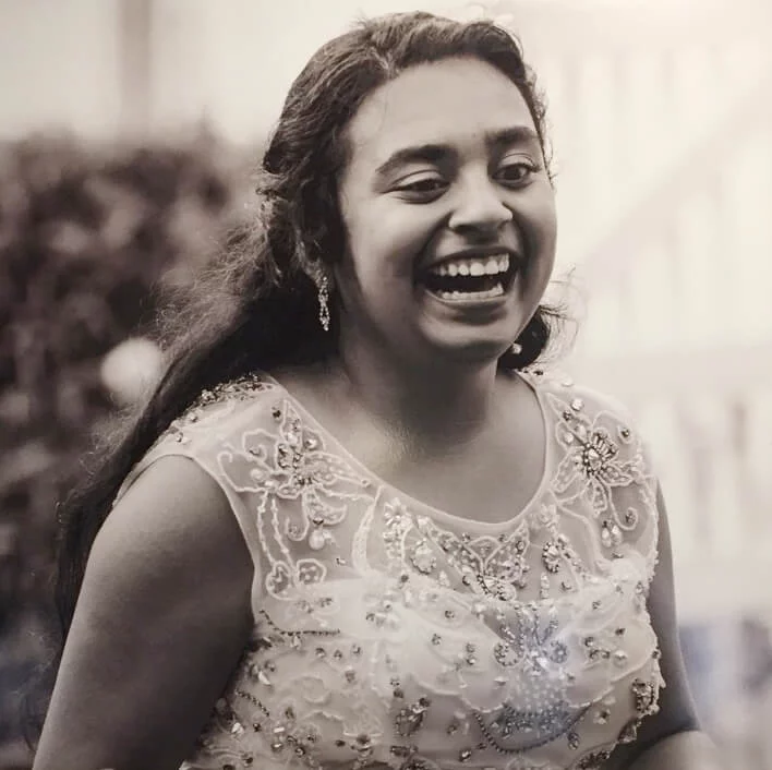 A girl with long hair, wearing a detailed, embellished dress, is joyfully laughing. The black-and-white image conveys a sense of happiness.