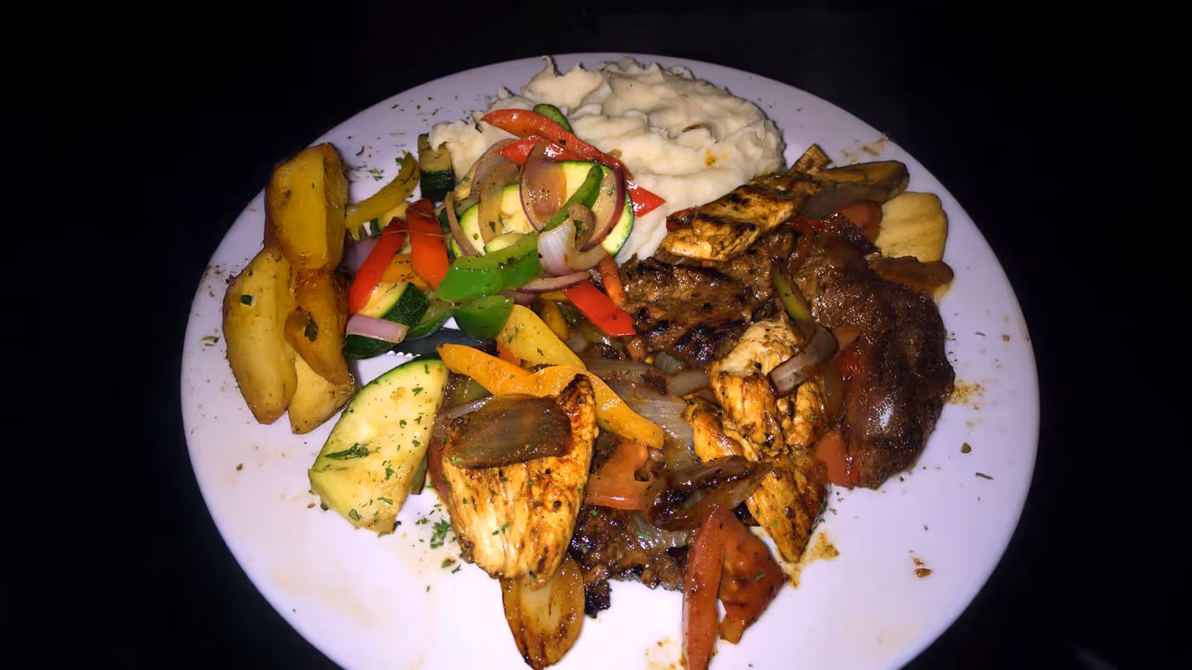 A plate of grilled meats, roasted vegetables, and mashed potatoes.