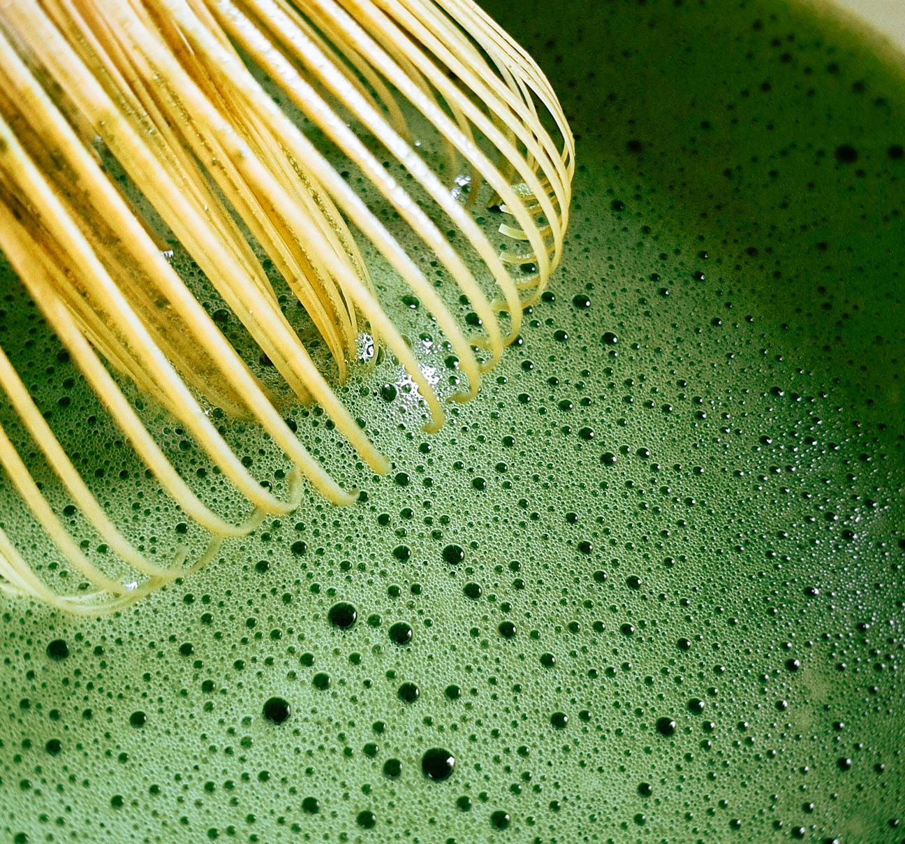 Close-up of frothy, vibrant green matcha tea in a bowl with a traditional bamboo whisk (chasen) resting on the surface.