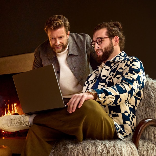 Two men looking at a laptop near a fireplace