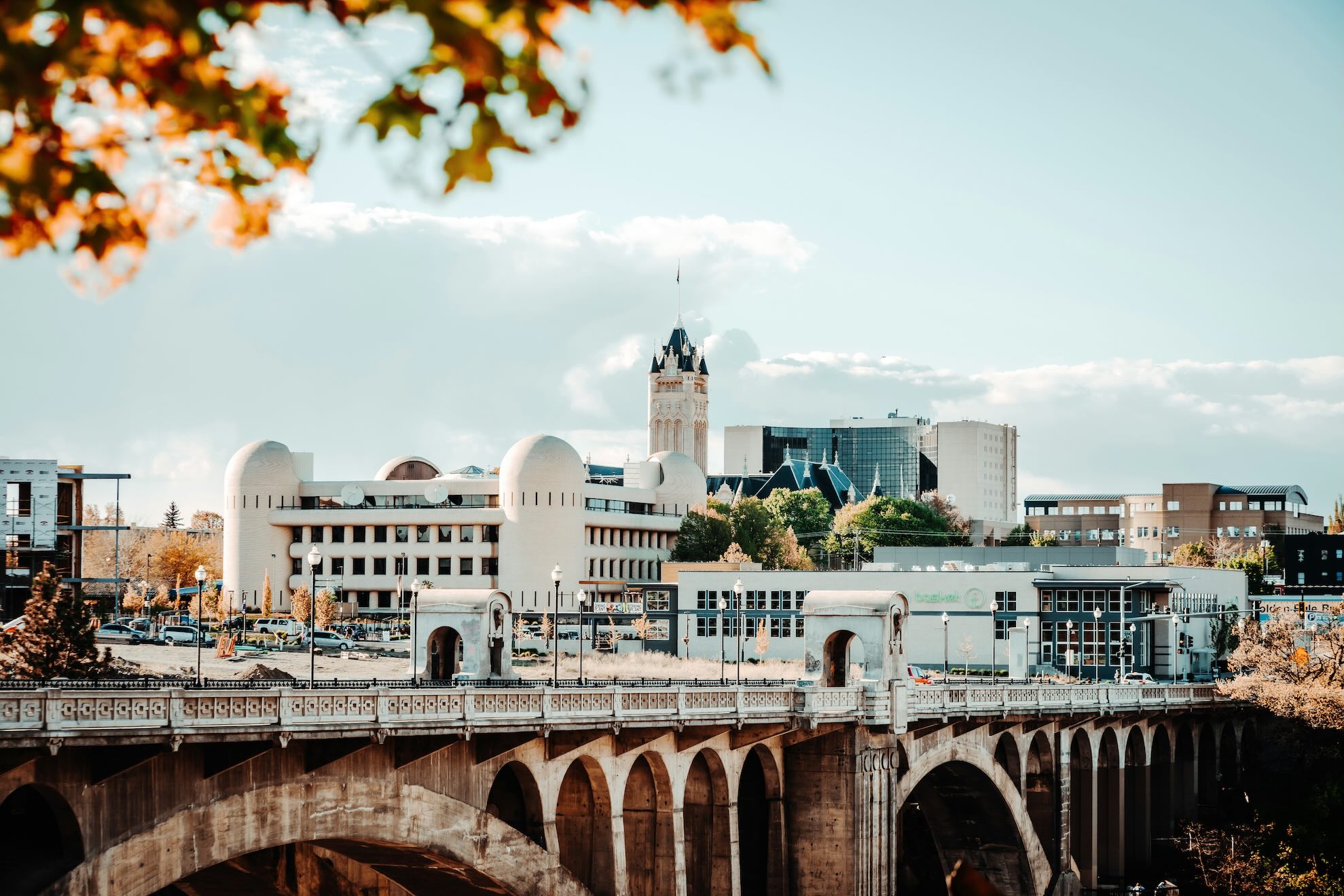 Spokane skyline with an arched river bridge in the foreground and a clock-tower in bright afternoon light.